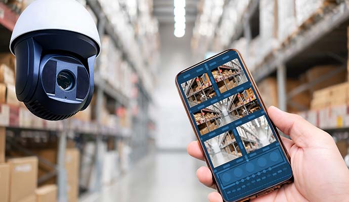 Smartphone displaying live warehouse surveillance camera feeds with a ceiling dome security camera