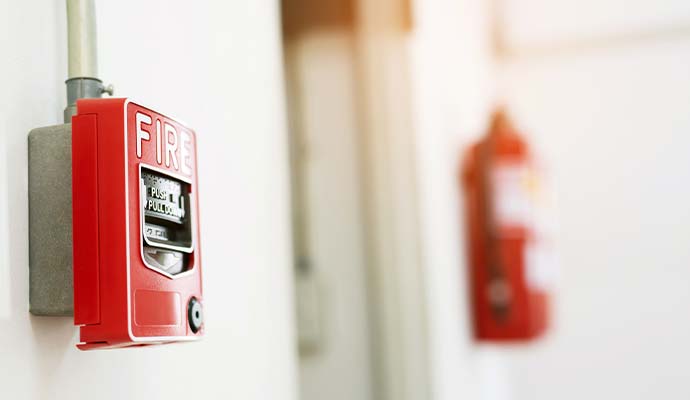 Emergency fire alarm pull box on a wall with a fire extinguisher in the background