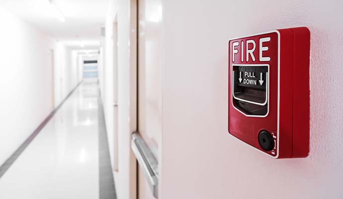 Red manual fire alarm pull station installed along a bright commercial hallway