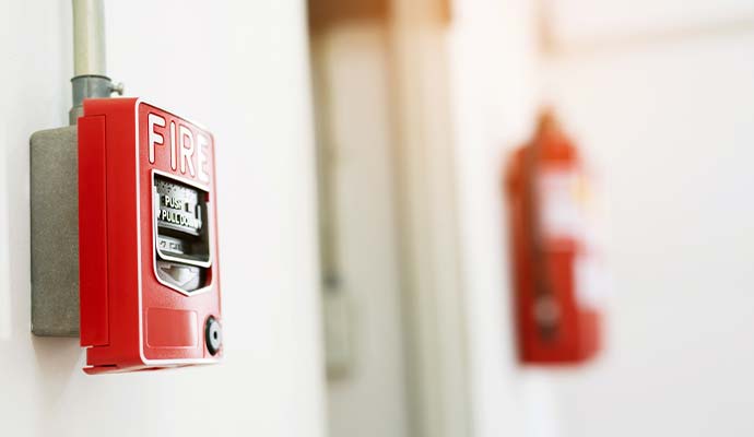 Red fire alarm pull station mounted on a wall with a fire extinguisher in the background