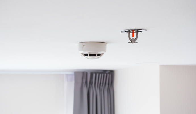 Smoke detector and fire sprinkler on white ceiling