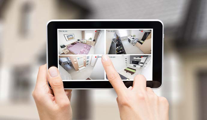 Hands holding a tablet displaying a 4-room live home security camera feed