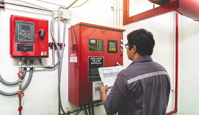 Technician reviewing an inspection checklist while examining an industrial fire pump controller