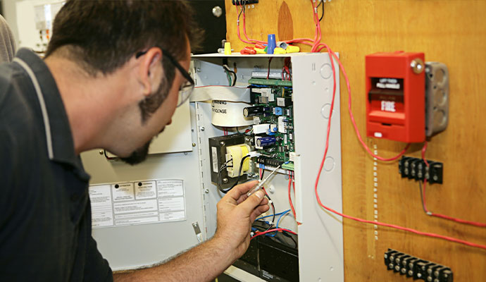 Technician servicing open fire alarm control panel