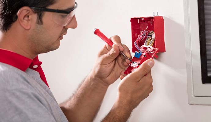 Technician wiring and installing a red commercial fire alarm station
