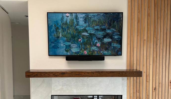 Framed art TV and soundbar mounted above fireplace