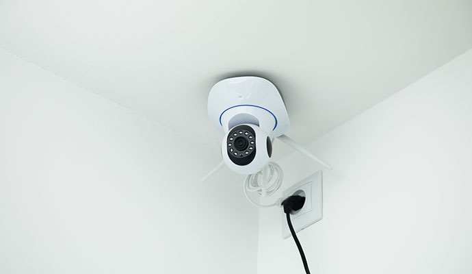 Indoor security camera mounted on a ceiling near a wall outlet.