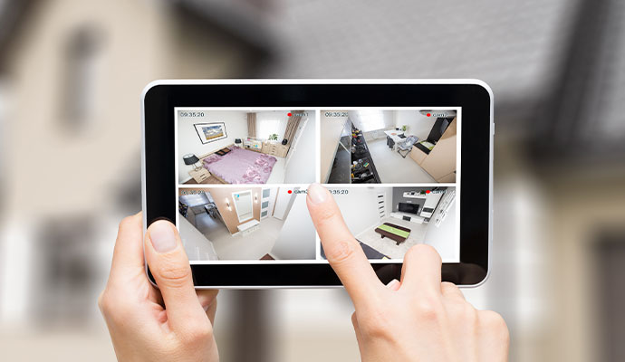Person monitoring four indoor security camera feeds on a tablet.